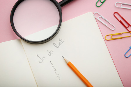To do list in notepad with pencil and magnifying glass on pink backgroundの写真素材