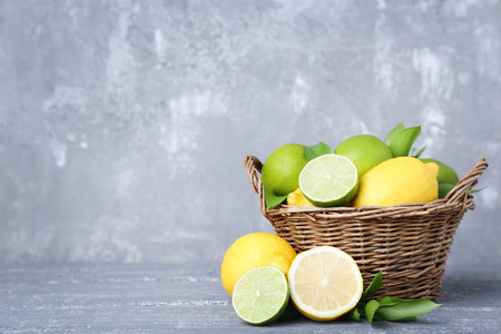 Lemons and limes with green leafs in basket on grey wooden tableの写真素材