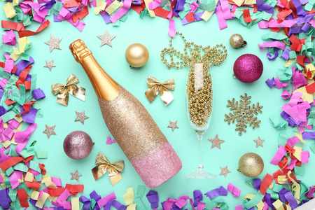 Champagne bottle with christmas decorations and confetti on mint background