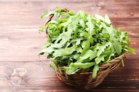 Green arugula leafs in basket on brown wooden tableの写真素材