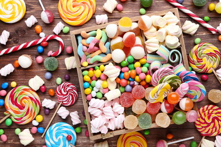 Sweet candies and lollipops in basket on brown wooden tableの写真素材