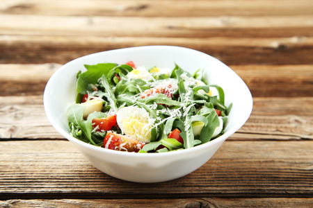 Salad with arugula leafs, tomatoes and eggs on brown wooden tableの写真素材