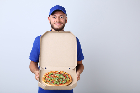 Delivery man with pizza in cardboard box on grey backgroundの写真素材