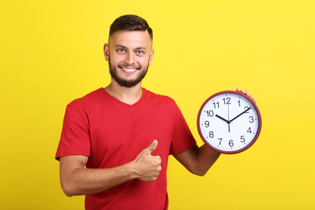 Young man with round clock on yellow backgroundの写真素材