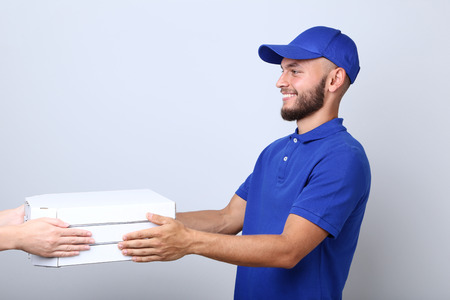 Delivery man with pizza in cardboard boxes on grey backgroundの写真素材