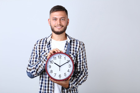 Young man with round clock on grey backgroundの写真素材