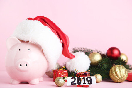 Pink piggybank in santa hat with christmas decorations on pink background