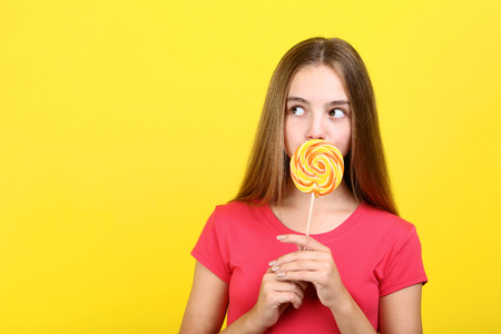 Young girl with lollipop on yellow backgroundの写真素材