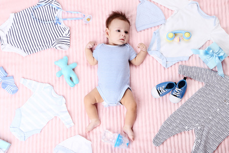 Cute baby with fashion clothes and toys lying on pink bedの写真素材