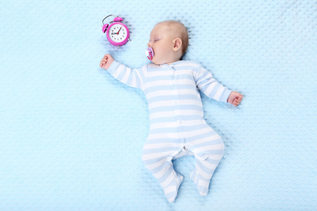 Baby boy with alarm clock sleeping in blue bedの写真素材