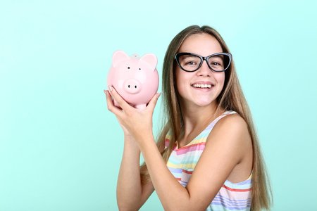 Young girl holding pink piggybank on mint backgroundの写真素材