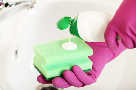 Hands in gloves with sponge and bottle of detergent cleaning water tap in bathroomの写真素材