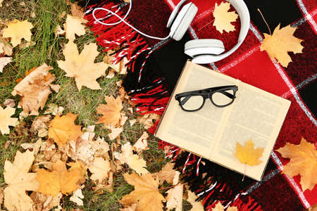 Opened book on plaid with glasses, headphones and dry autumn leafsの写真素材