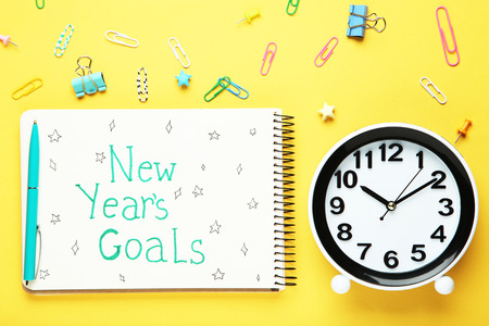 New year goals in notepad with round watch and paper clips on yellow background