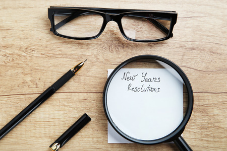 New year resolutions on sheet of paper with glasses, pen and magnifying glass