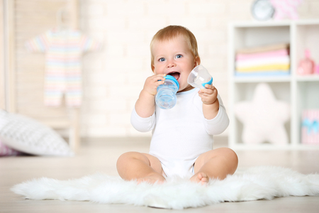 Baby boy drinking water from bottle and sitting on carpet at homeの写真素材