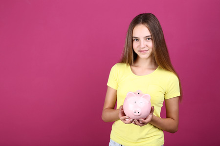 Young girl holding pink piggybank on pink backgroundの写真素材