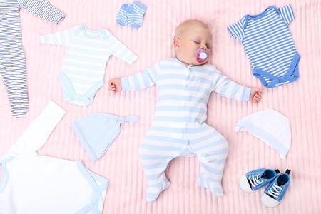 Baby boy with fashion clothes lying on pink bedの写真素材
