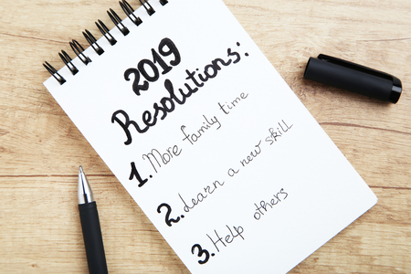 Inscription 2019 resolutions in notepad with pen on wooden tableの写真素材