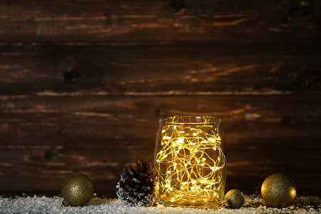 Garland lights in glass jar with Christmas baubles and cone on brown background