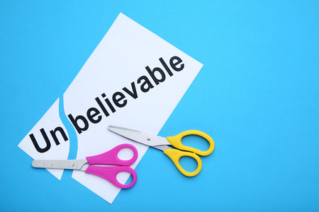 Paper with word Unbelievable and colorful scissors on blue background
