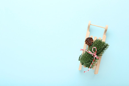 Wooden sleigh with fir tree branches and cone on blue background