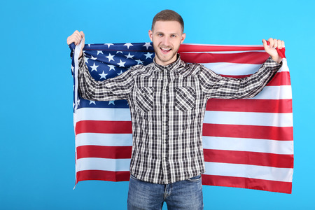 Young man holding an American flag on blue backgroundの写真素材