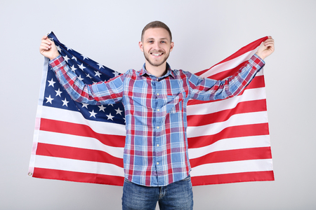 Young man holding an American flag on grey backgroundの写真素材