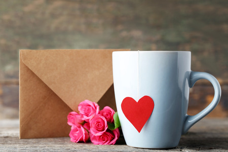 Cup of tea with roses and envelope on wooden tableの写真素材