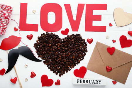 Heart shape made from coffee beans with inscription Love and red hearts on white wooden tableの写真素材