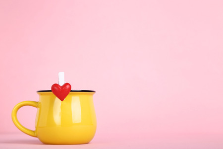 Yellow cup and clothespin with red heart on pink backgroundの写真素材