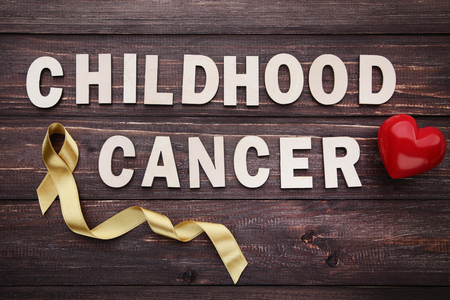 Golden ribbon with inscription and red heart. Children cancer conceptの写真素材