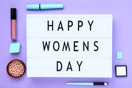Lightbox with words Happy Womens Day and makeup cosmetics on purple backgroundの写真素材