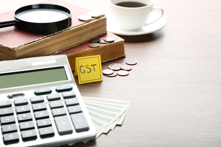 Inscription GST on paper with coins, banknotes, calculator and booksの写真素材