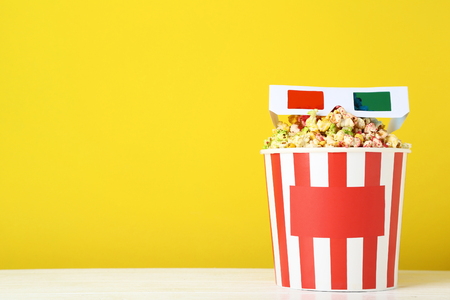 Sweet popcorn in striped bucket with glasses on yellow backgroundの写真素材