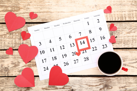 Valentine day calendar with paper hearts and cup of coffee on wooden tableの写真素材