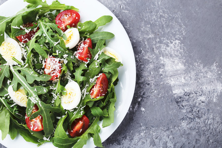 Salad with arugula leafs, tomatoes and eggs on grey wooden table