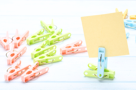 Colorful plastic clothespins with blank sheet of paper on wooden tableの写真素材