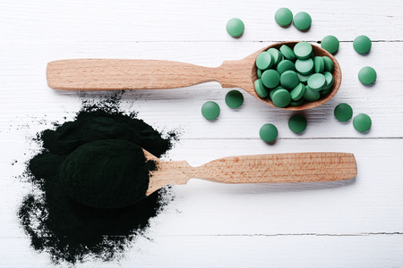 Spirulina powder and tablets in spoons on wooden tableの写真素材