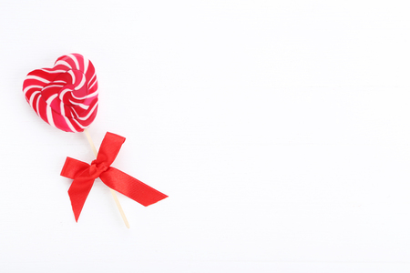 Heart shaped lollipop with red ribbon bow on white wooden tableの写真素材