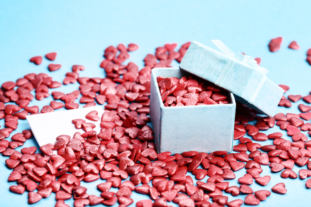 Red heart shaped sprinkles with gift box on blue backgroundの写真素材
