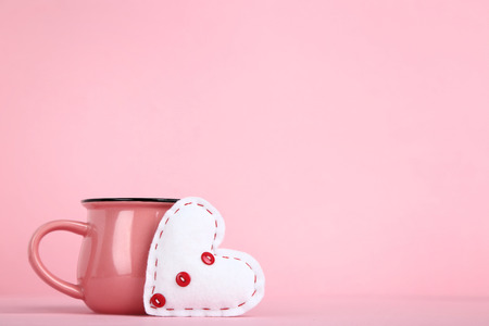 White fabric heart with cup on pink backgroundの写真素材