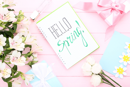Fresh flowers, gift boxes and notepad with text Hello Spring on pink wooden tableの写真素材