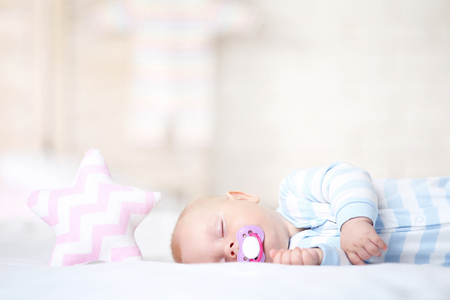 Baby boy with soother and soft star toy sleeping in bed at homeの写真素材