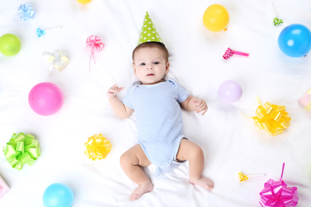Cute baby with birthday decorations lying on white bedの写真素材