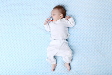 Cute baby with soother lying on bed