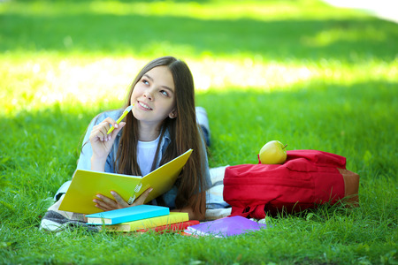 Cute girl lying with notebook and books in the parkの写真素材