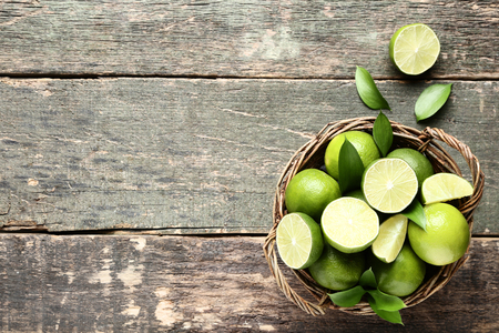 Ripe limes in basket on grey wooden tableの写真素材