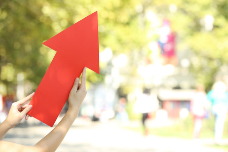 Female hands holding red paper arrow on the streetの写真素材