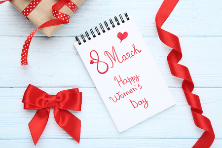 Text Happy Women's Day in notepad with gift box and ribbon bowの写真素材